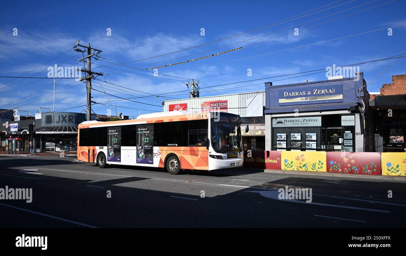 Volvo B7RLE bus, operated by Ventura and featuring current PTV livery, driving through a pocket of sunshine along the Centre Rd shopping strip Stock Photo