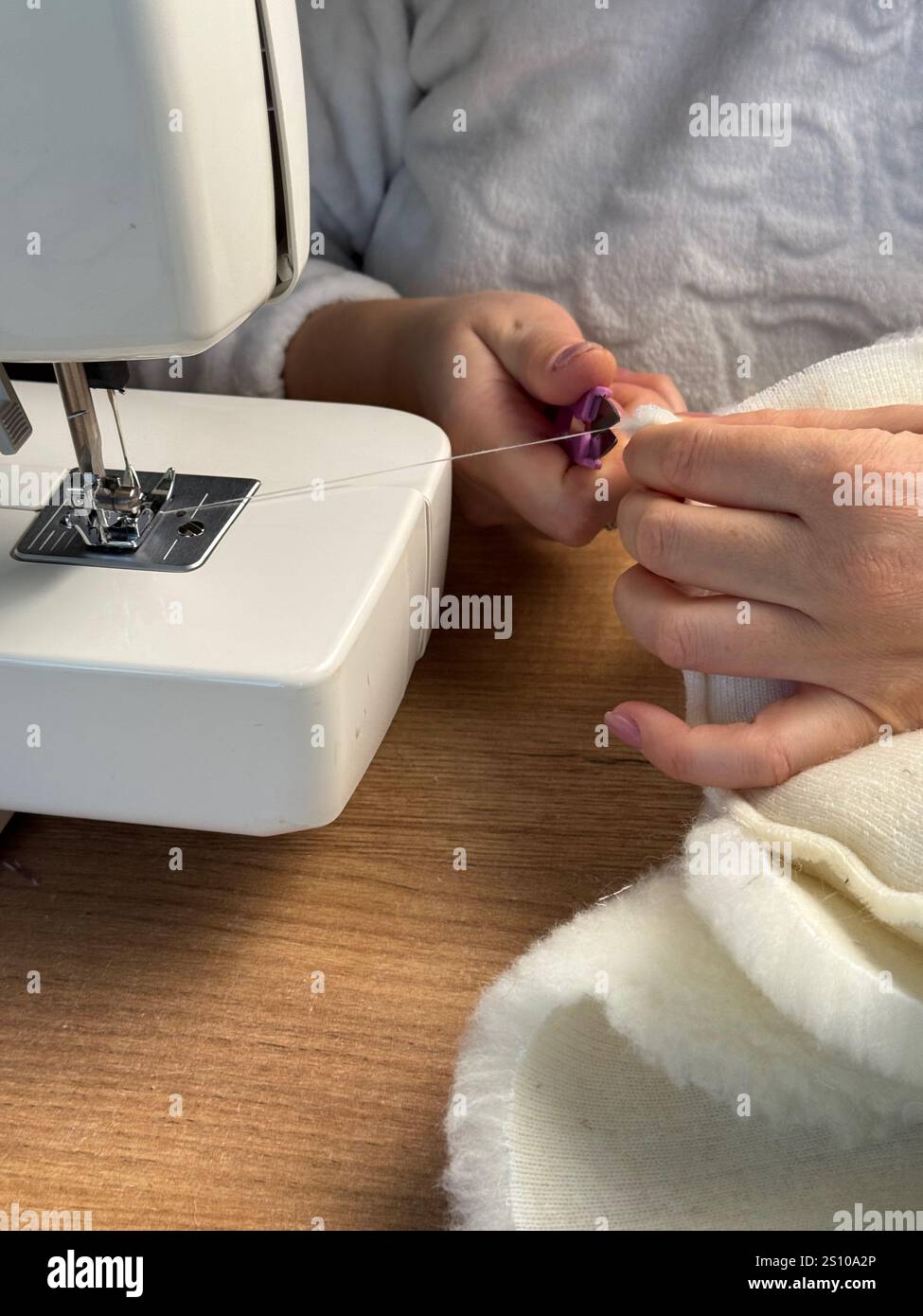 The woman cuts the thread with scissors. She is sewing a pet bed from fur fabric. Stock Photo