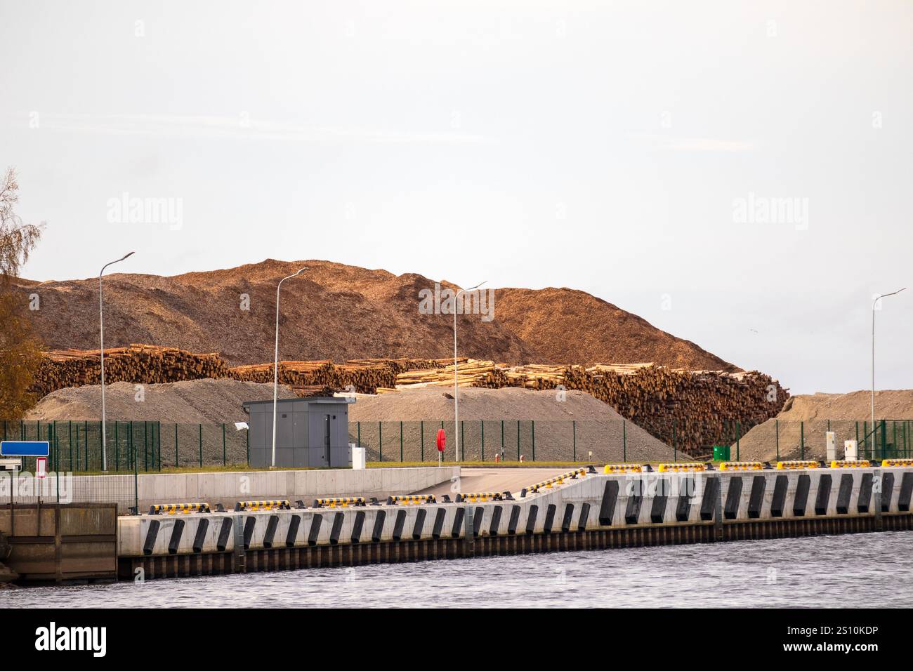 An industrial stretch of harbor shore with a large pile of wood chips ...
