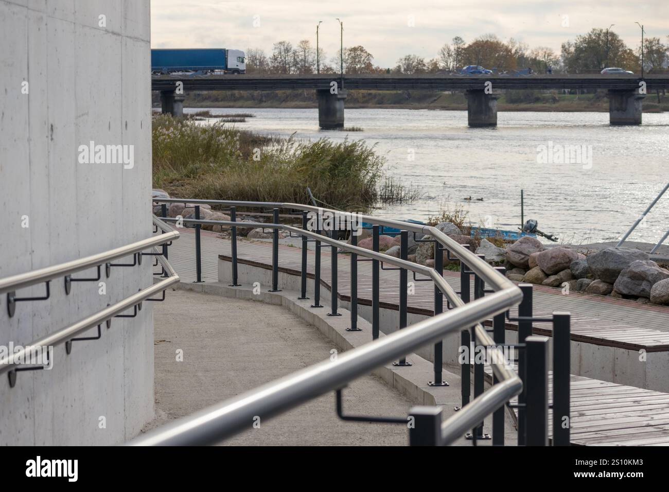 River bank with concrete promenade and metal railings. A bridge over ...