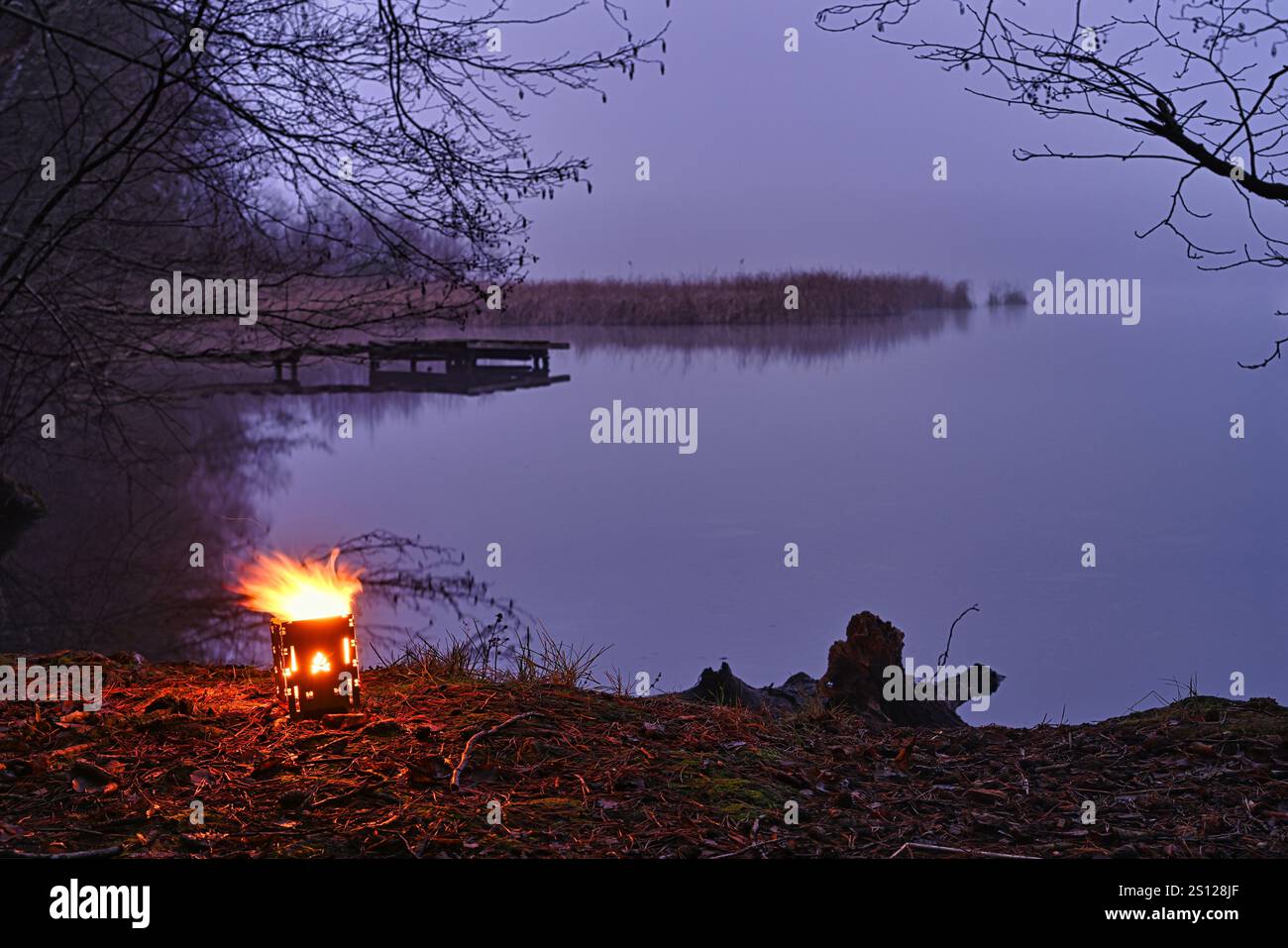 Bushbox burns by a lake in the fog. Stock Photo