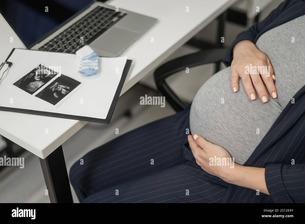 A pregnant woman works on a laptop in the office and looks at a photo ...