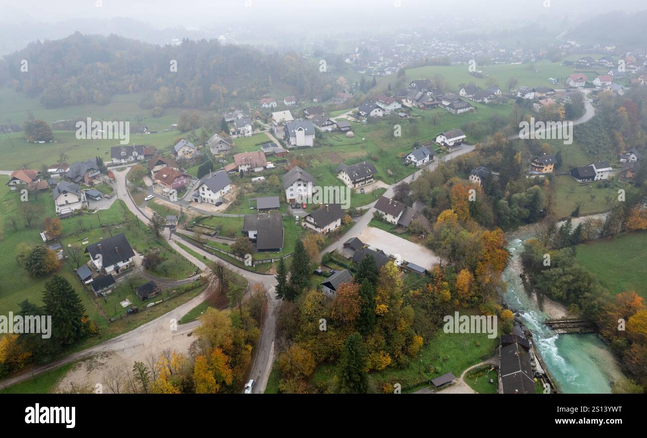 Drone Aerial view of houses in the countryside near a river surrounded by colorful autumn trees and fog, Podhom village radovna valley Slovenia Stock Photo