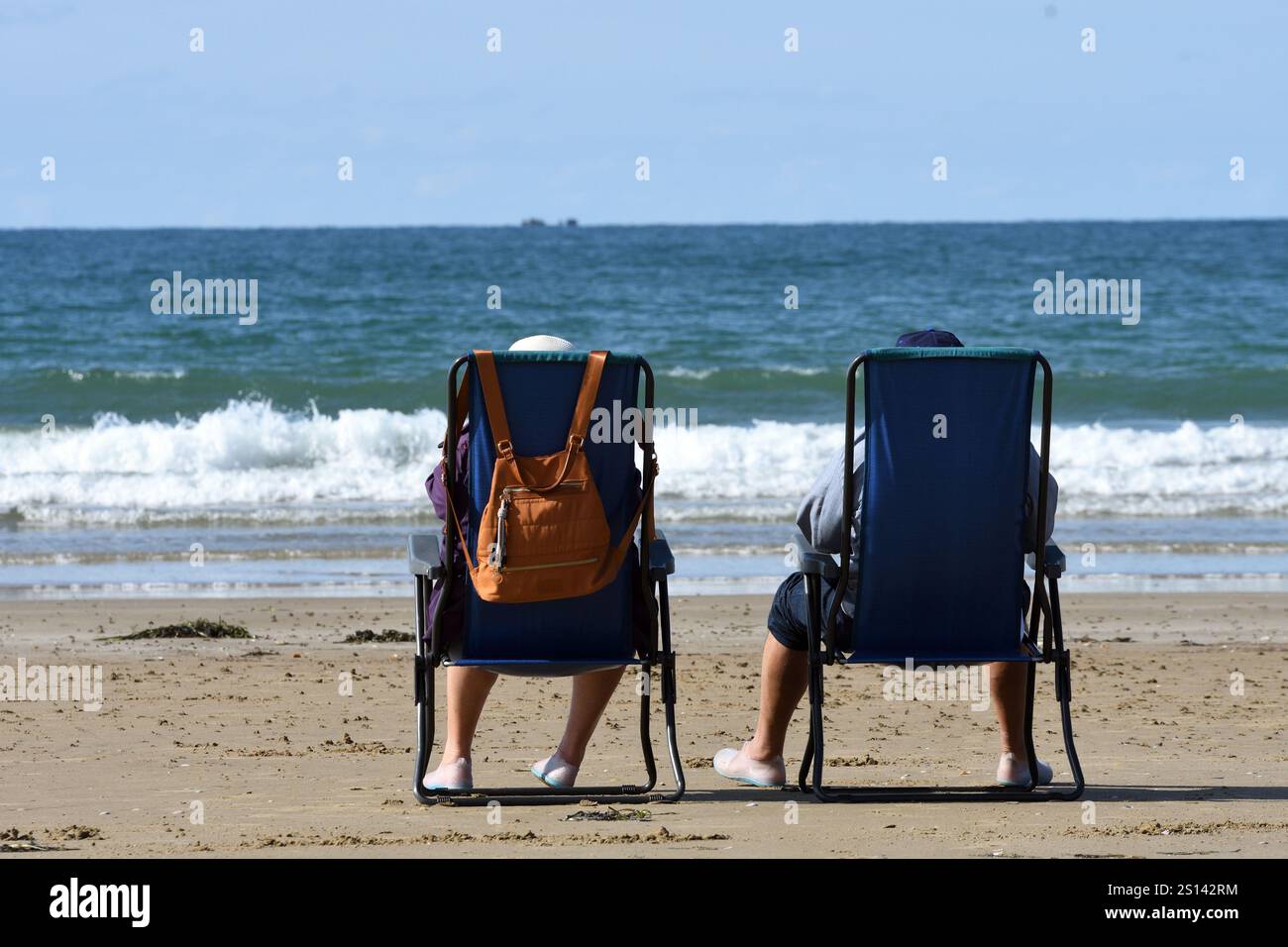 couple sitting in camping chairs on the beach looking out to sea, France, Brittany, Erquy Stock Photo