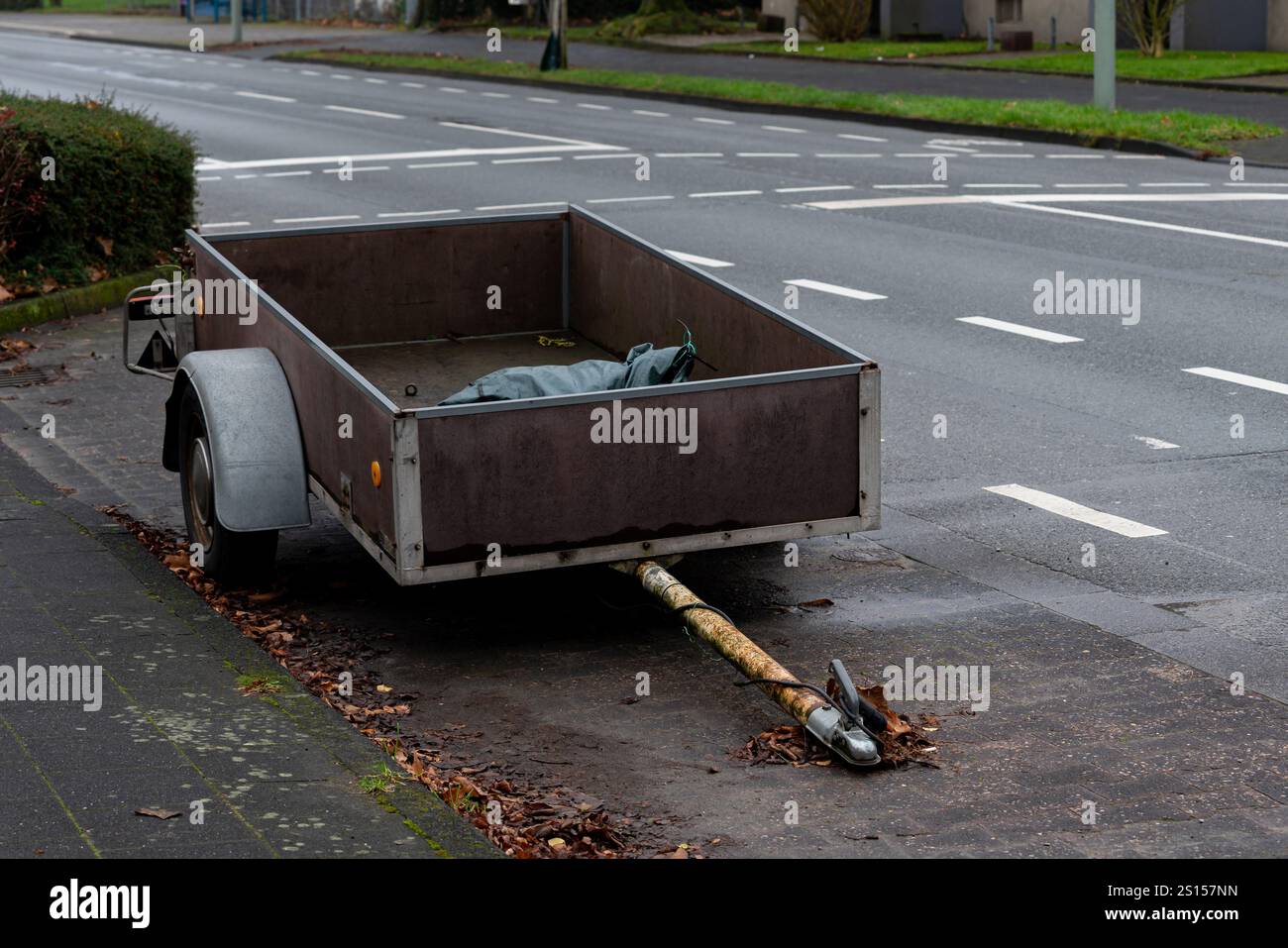 A neglected trailer rests on the side of a quiet suburban road. The