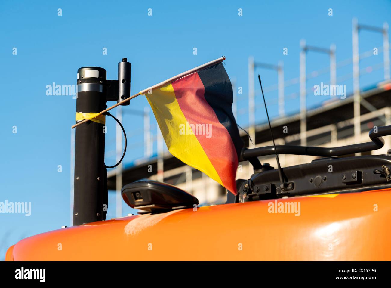 A construction vehicle is parked under a clear blue sky, displaying a small German flag. The modern city skyline rises in the background, showcasing o Stock Photo