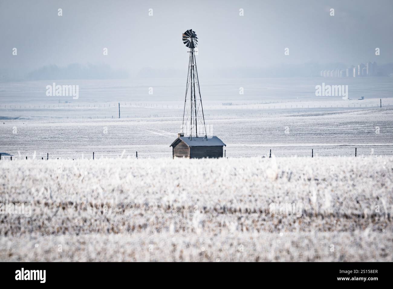 Old farm windmill standing next to shed on snow covered grasslands on a cold winter day in Rocky View County Alberta Canada. Stock Photo