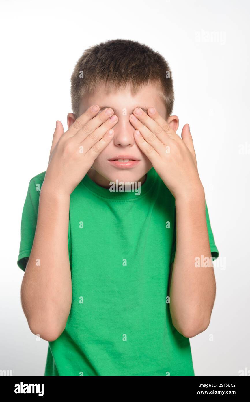 A young boy with short brown hair is shown covering his eyes with his ...