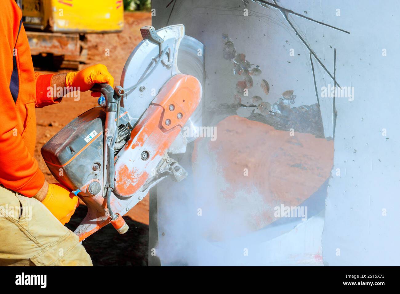 Worker uses concrete cutter, shaping drainage system creating dust on ...