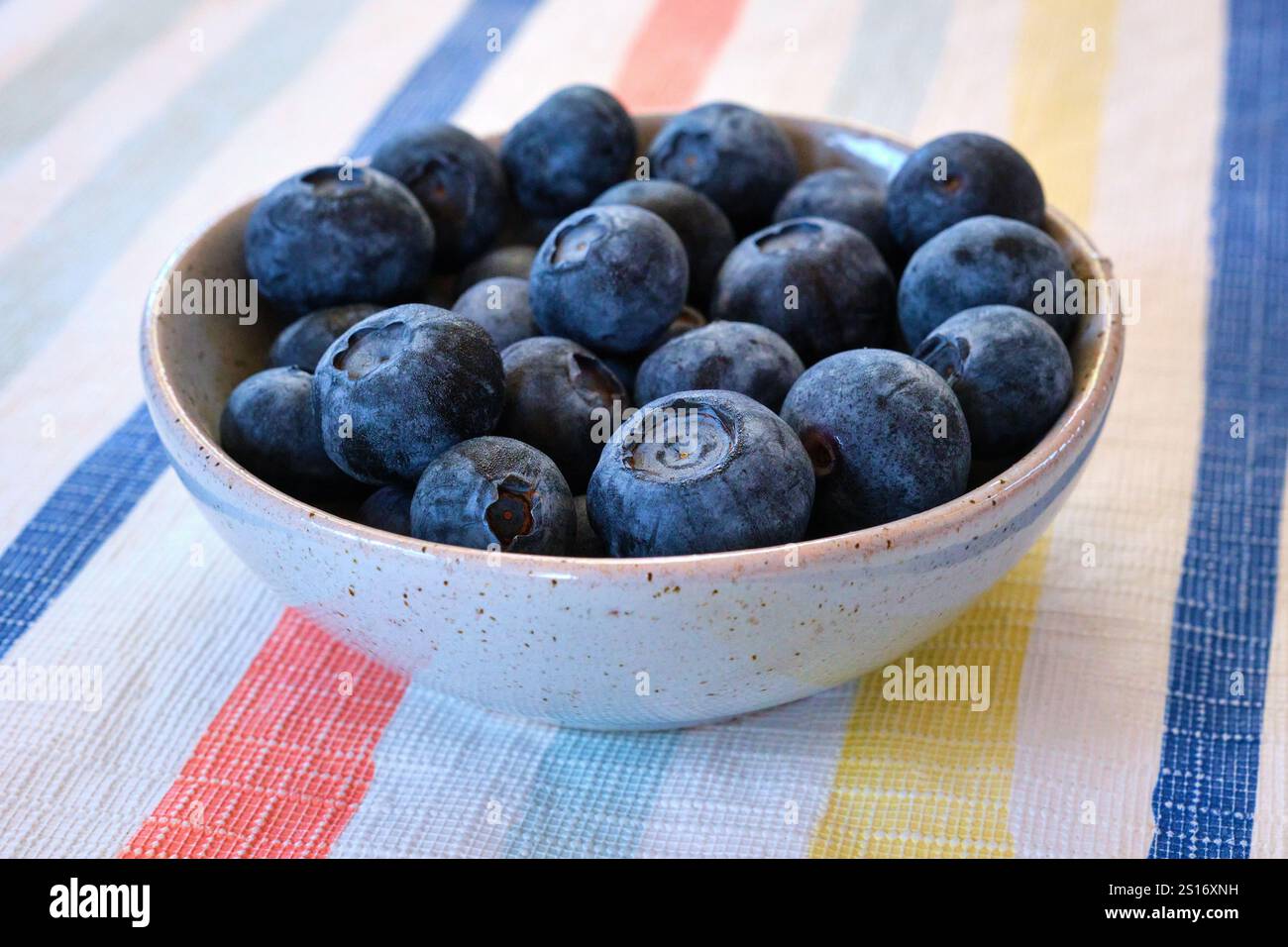 Fresh blueberries in a round bowl on a striped table cloth, a healthy fruit high in nutrients with a range of health benefits. Stock Photo