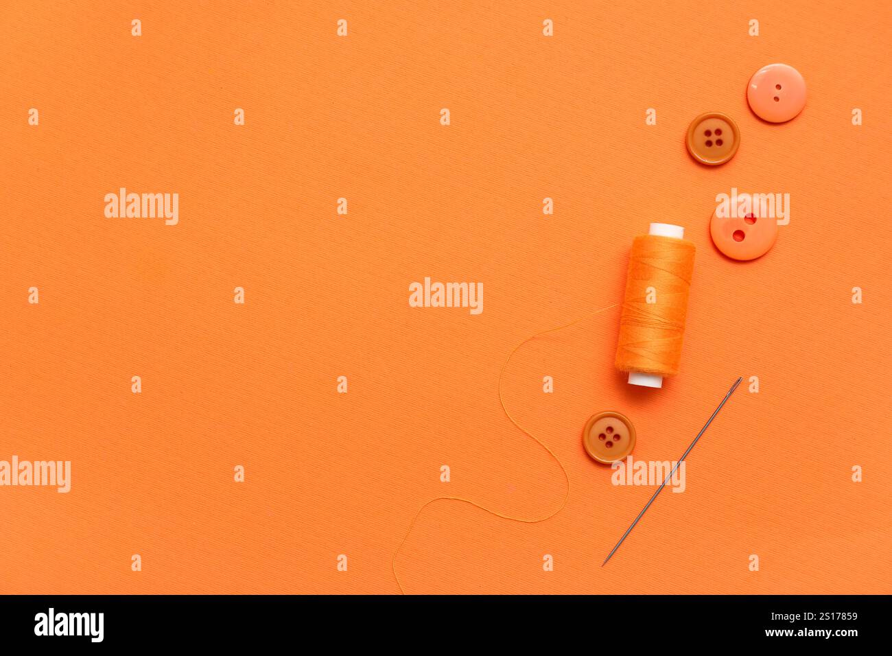 Thread spool, needle and buttons on orange background Stock Photo