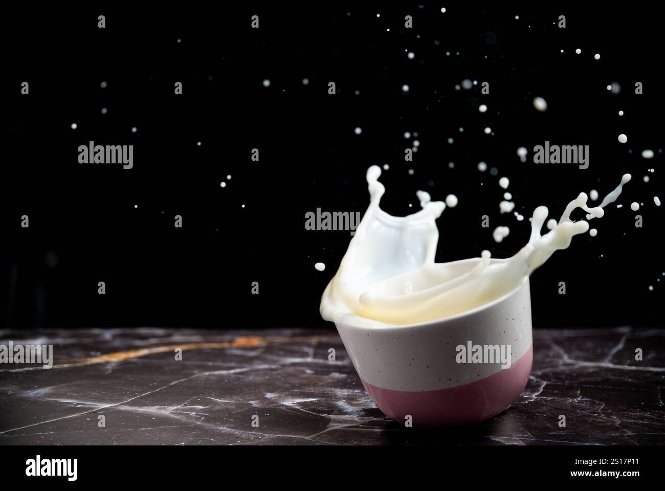 Milk Splash from the bowl on a black background. Dairy concept. No-dairy vegan plant milk splashes in bowl. Copy space. Stock Photo