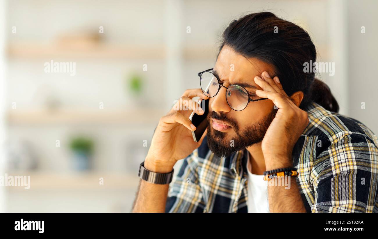 Upset middle-eastern guy having phone conversation, home interior Stock Photo