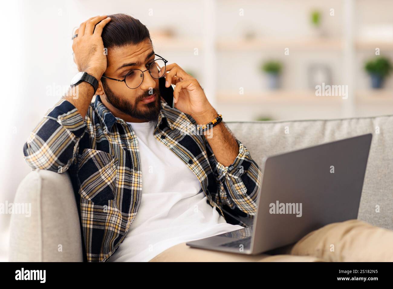 Stressful indian guy with laptop having phone conversation Stock Photo