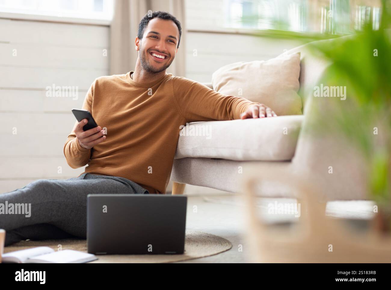 Young Arab man holding phone using pc at home Stock Photo