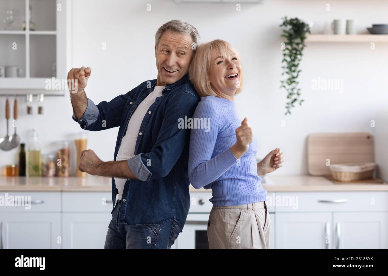 Joyful elderly spouses dancing together at kitchen Stock Photo