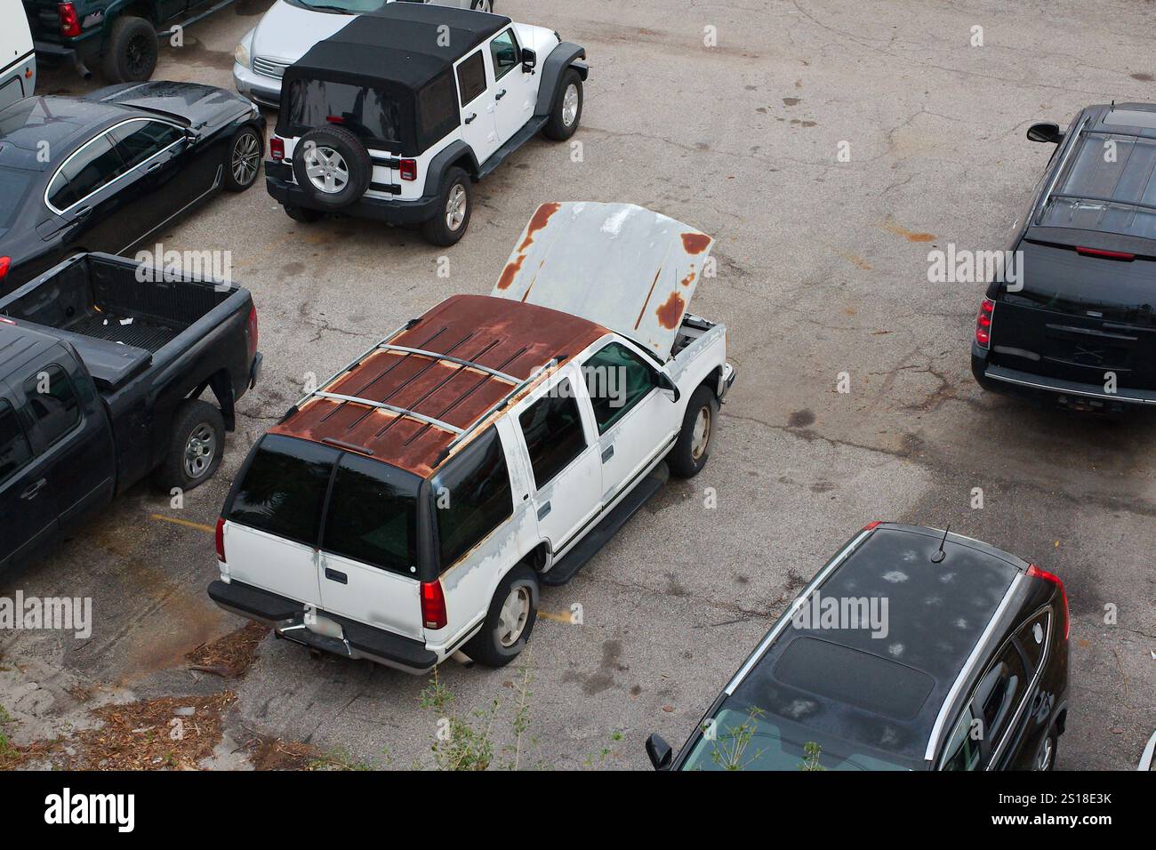 High View over an old white rusted SUV in a parking lot with other cars ...