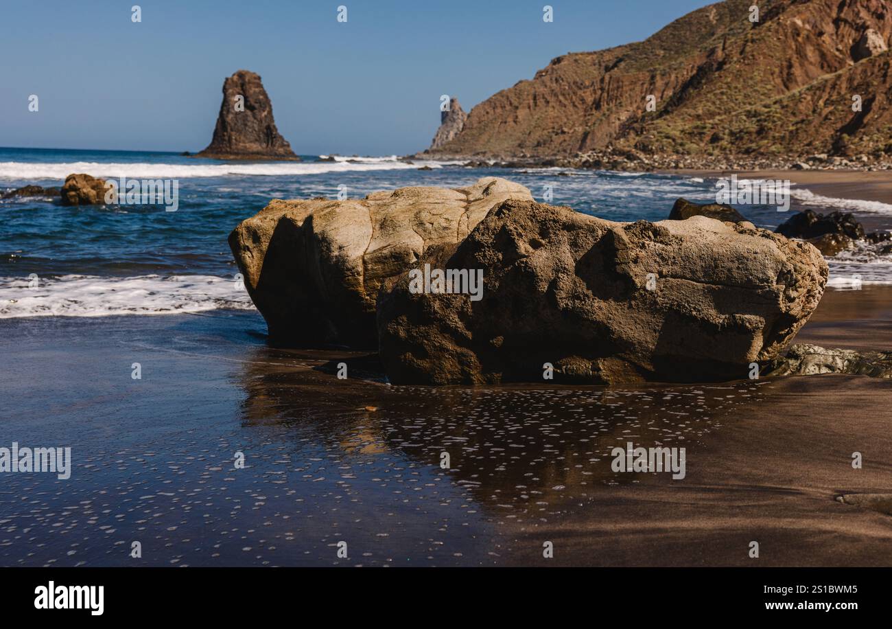 Rocky coastline with large boulders on a sandy beach, gentle waves, and ...