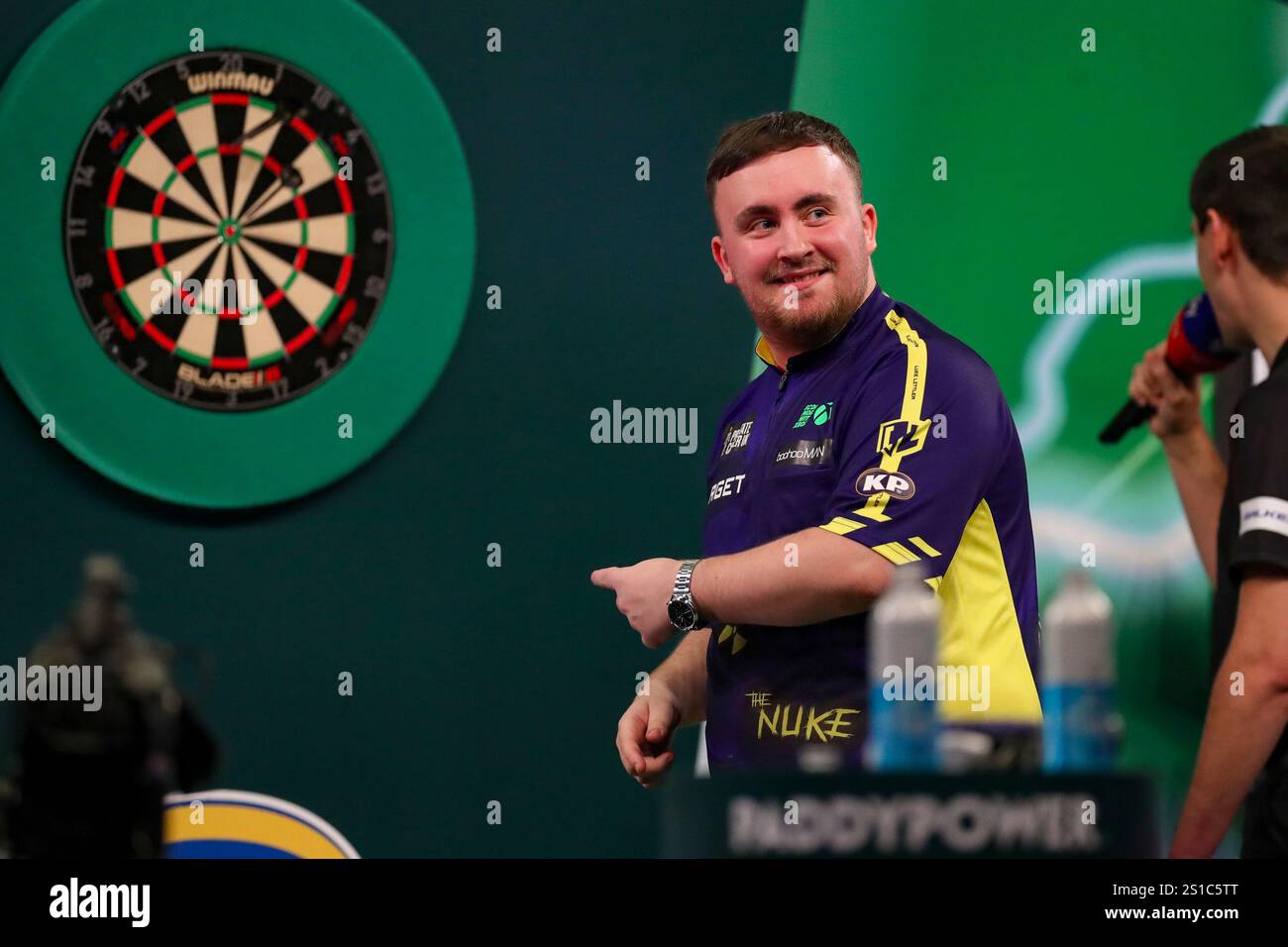 Luke Littler throws at the dart board and smiles reacts during the