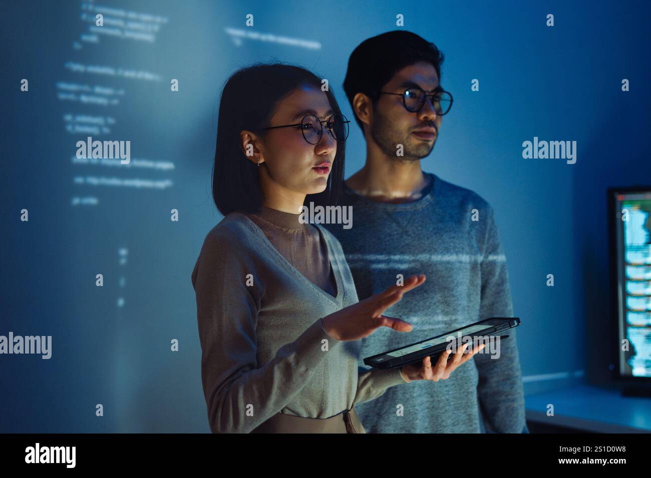 Asian Two software developers engaged in collaborative coding session, with code projected onto the wall and multiple computer screens displaying Stock Photo