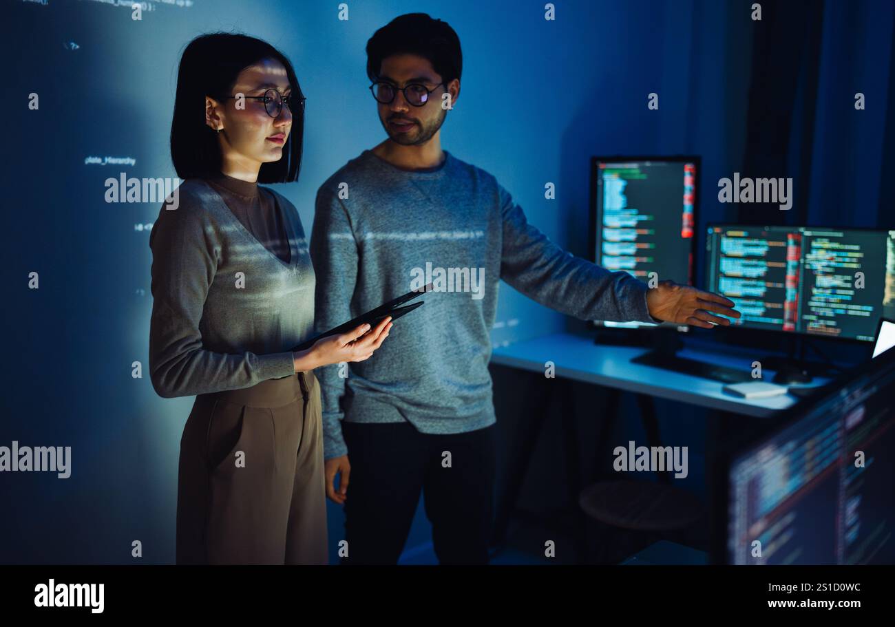 Asian Two software developers engaged in collaborative coding session, with code projected onto the wall and multiple computer screens displaying Stock Photo