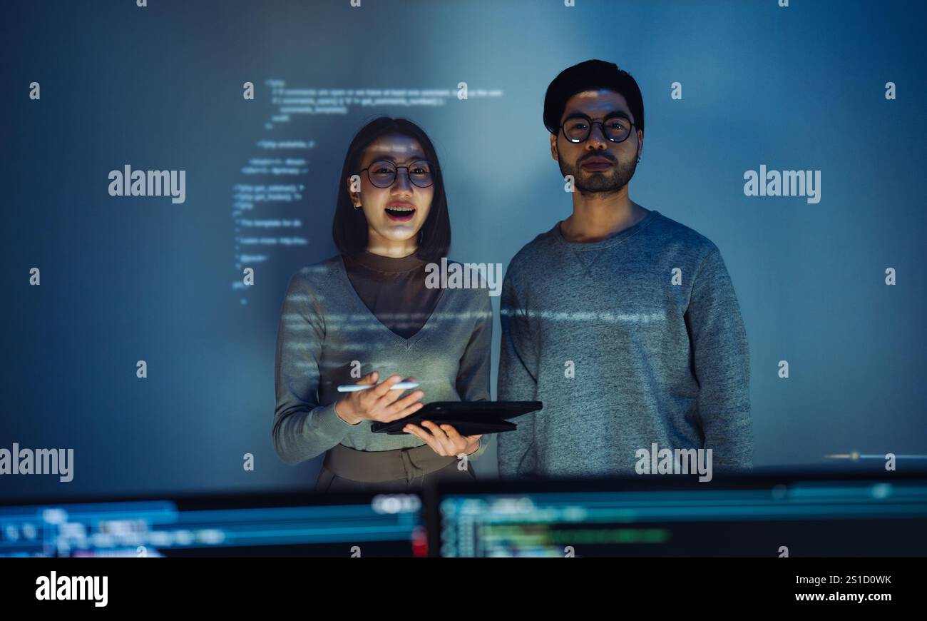 Asian Two software developers engaged in collaborative coding session, with code projected onto the wall and multiple computer screens displaying Stock Photo