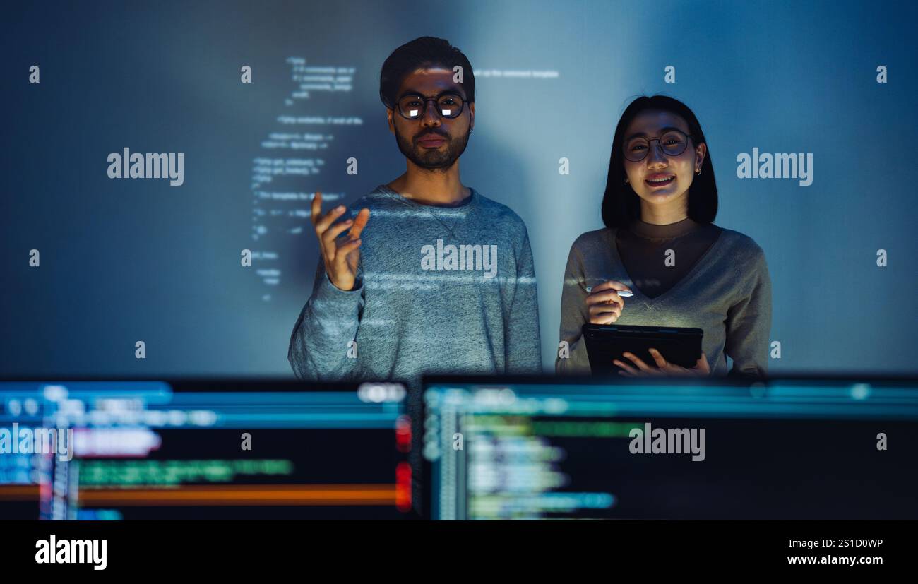 Asian Two software developers engaged in collaborative coding session, with code projected onto the wall and multiple computer screens displaying Stock Photo