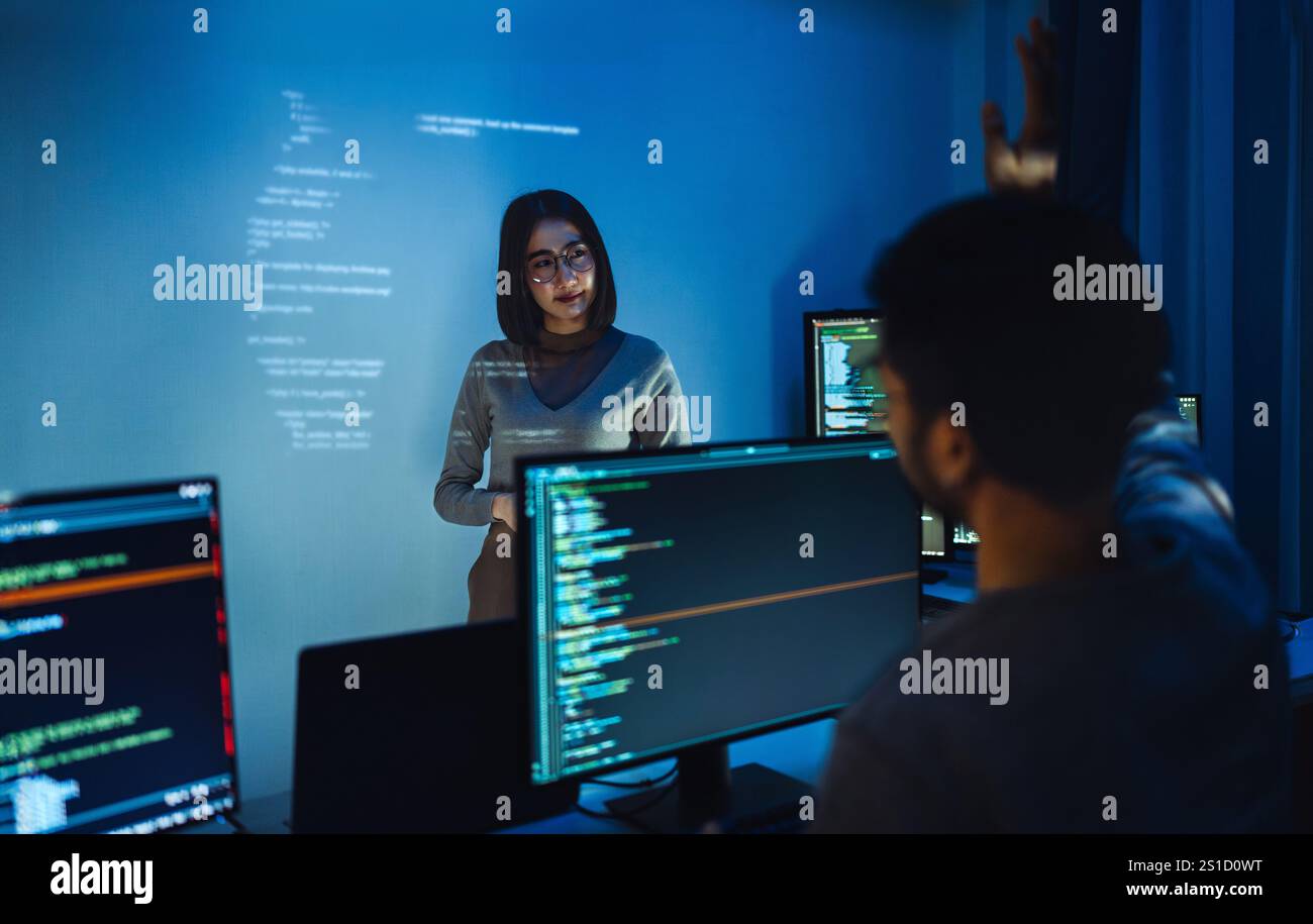 asian woman developers collaborating on a coding project, with one member presentation at code projected on the wall while the other works on multiple Stock Photo