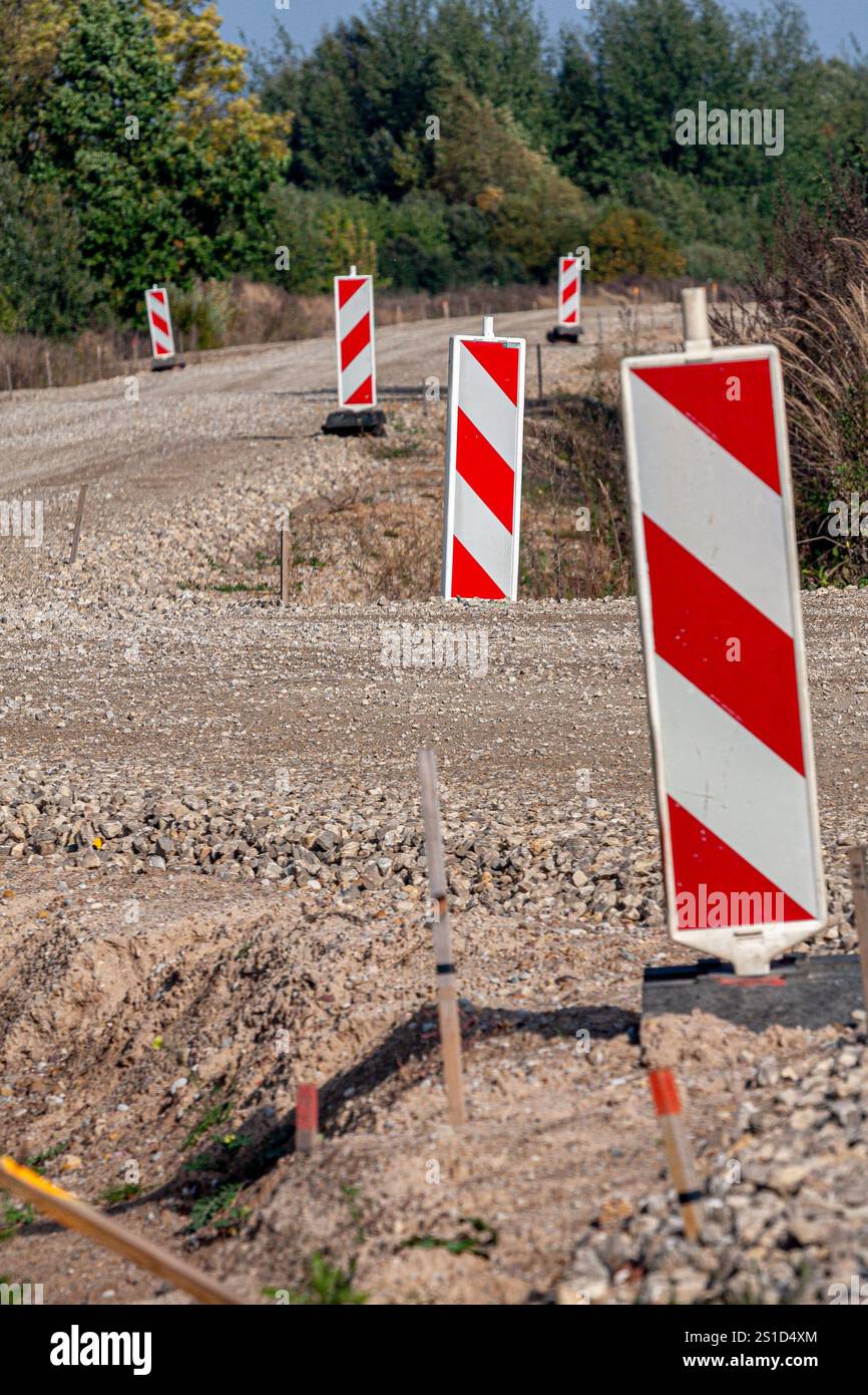 Construction site of a gravel road lined with red-and-white traffic diversion signs amidst natural surroundings. Stock Photo