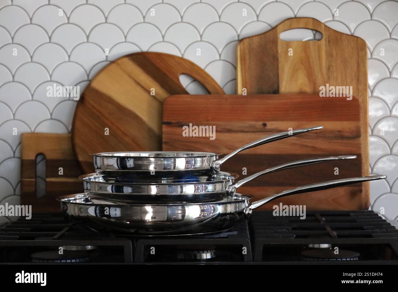 Stacked frying pans on stove with wooden boards in background Stock Photo