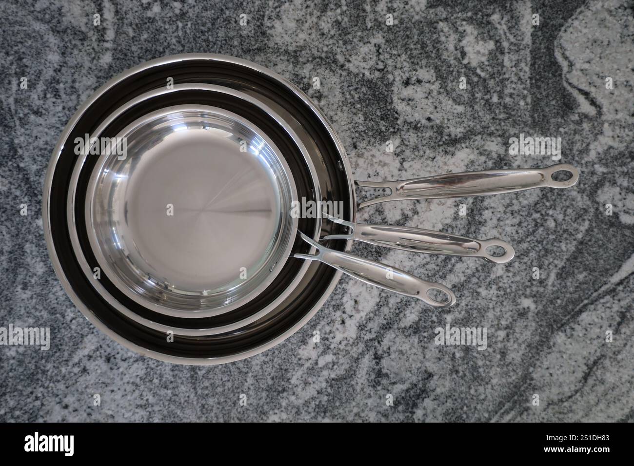Nesting stainless steel frying pans on granite countertop Stock Photo