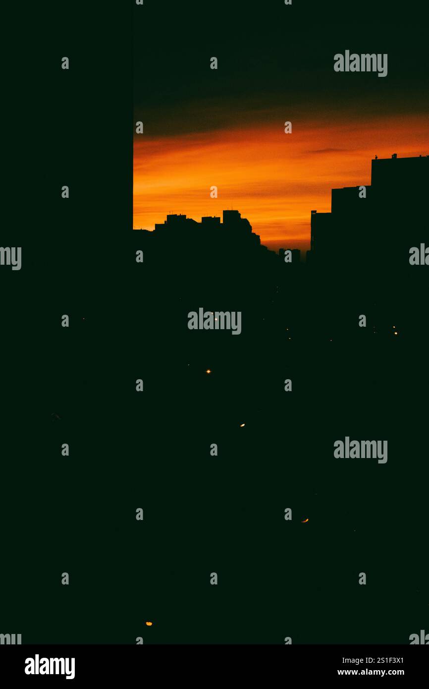 Abstract cityscape at sunset with bright orange sky and silhouettes of ...