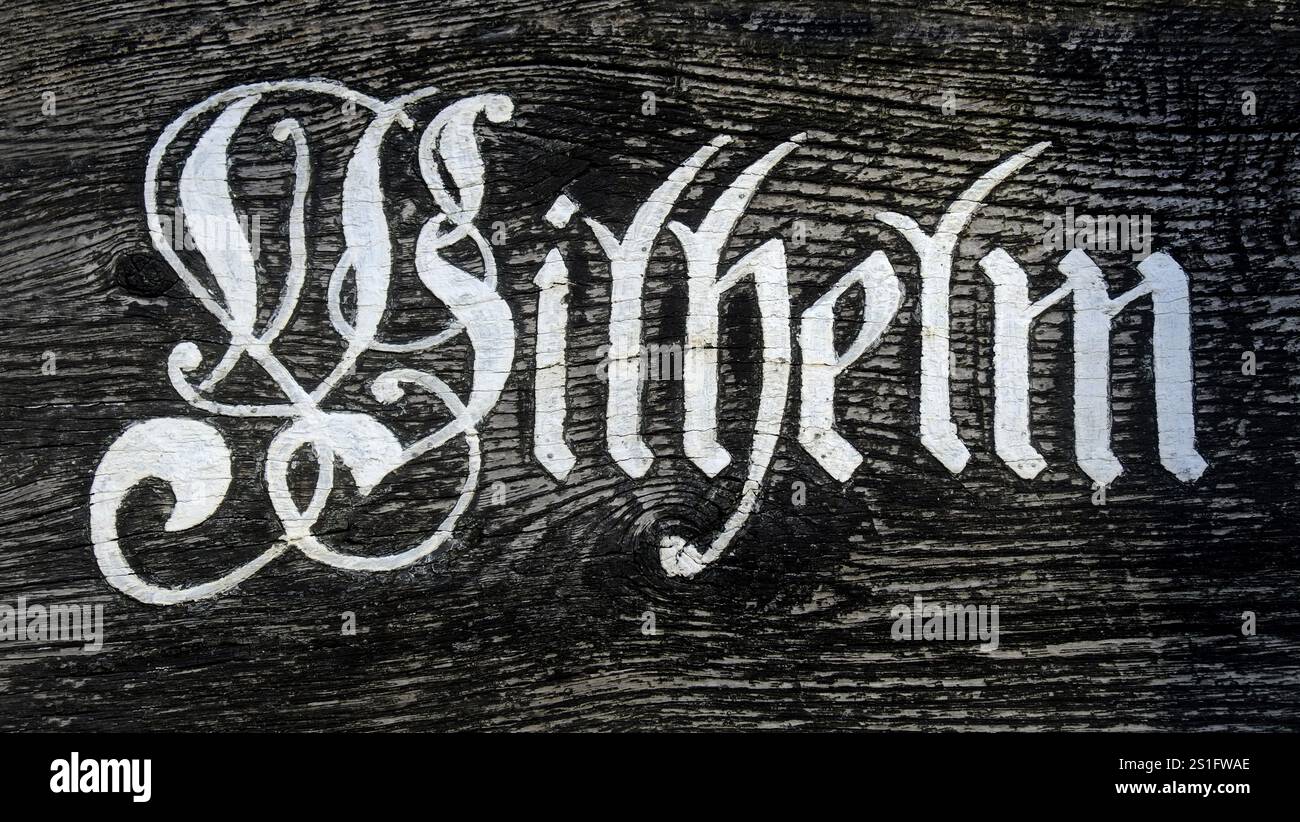 Wilhelm ? Hand-painted white letters in Fraktur script on a black wooden beam. Landscape format. Wilhelm lettering: hand-painted white letters in Goth Stock Photo