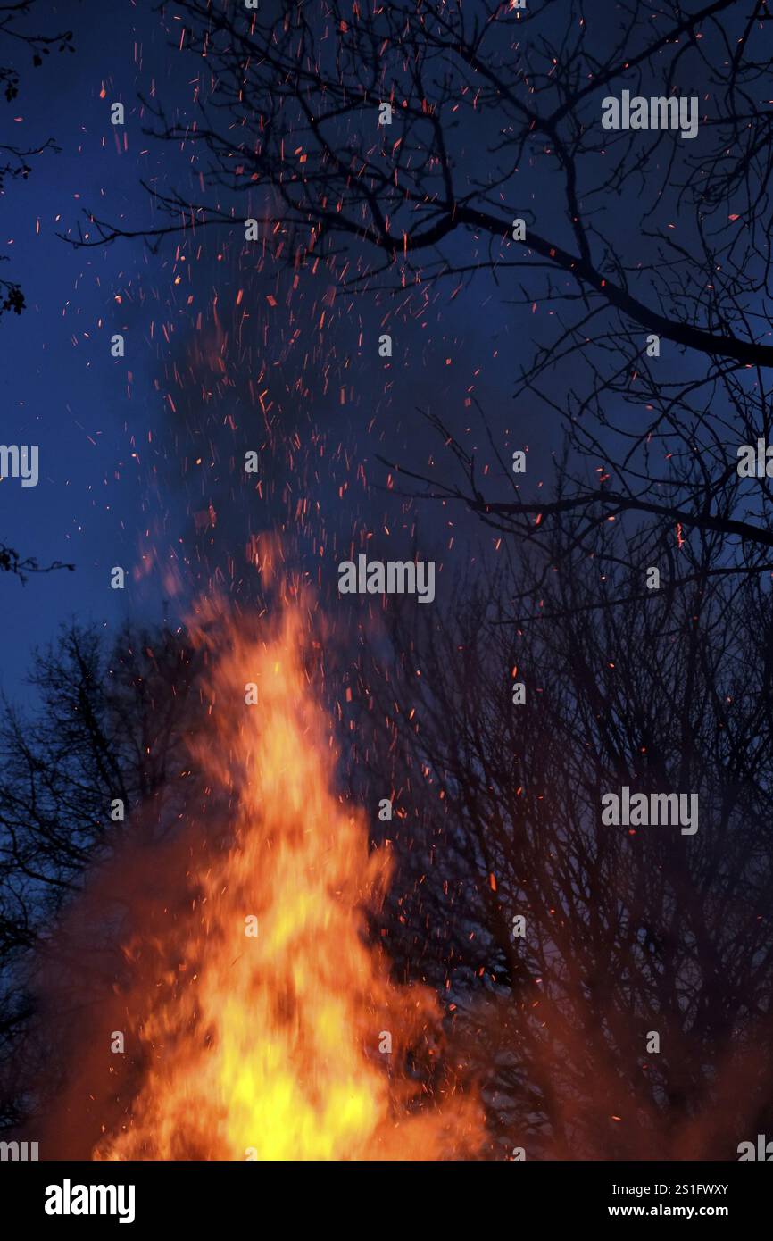 Crackling flames and red-hot flying sparks against a black-blue night sky. Portrait format. Crackling flames and red-hot sparks in front of black-blue Stock Photo