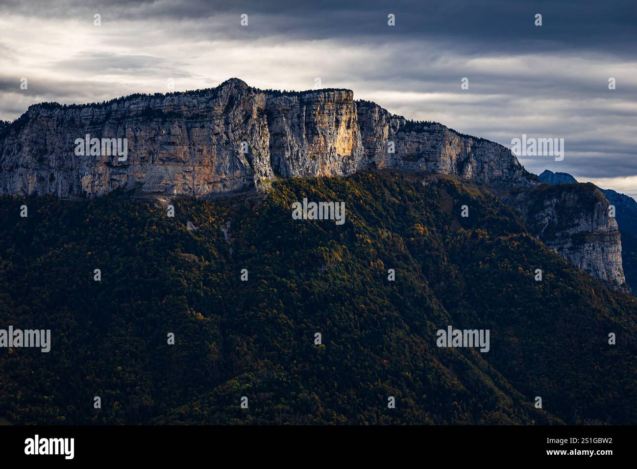 Mountain views of cliff face with sun peeking out from the clouds, while hiking above Annecy, France on a moody and cloudy autumn day Stock Photo