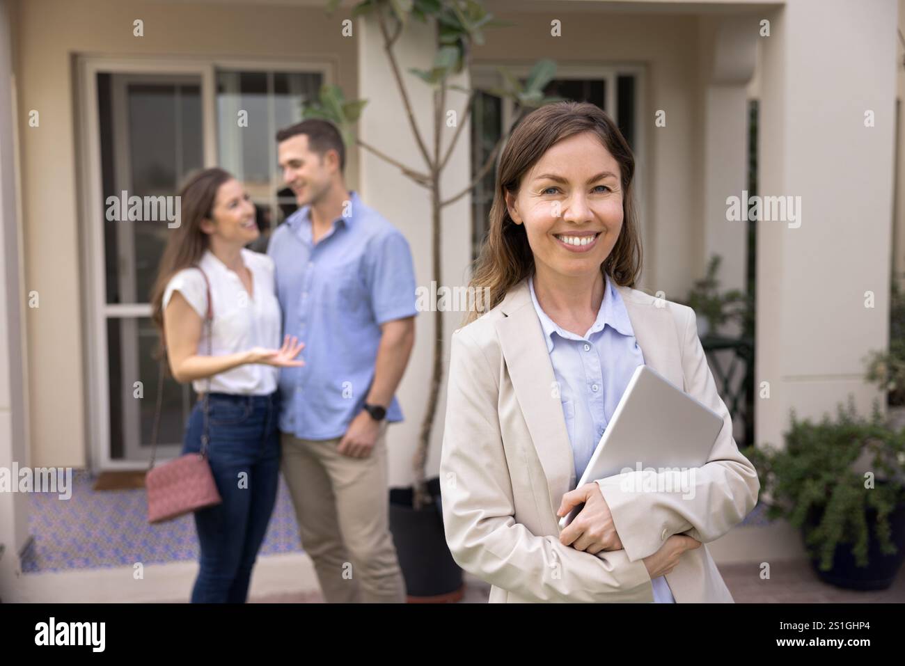 Happy realtor posing outdoors with accommodation and renters in background Stock Photo