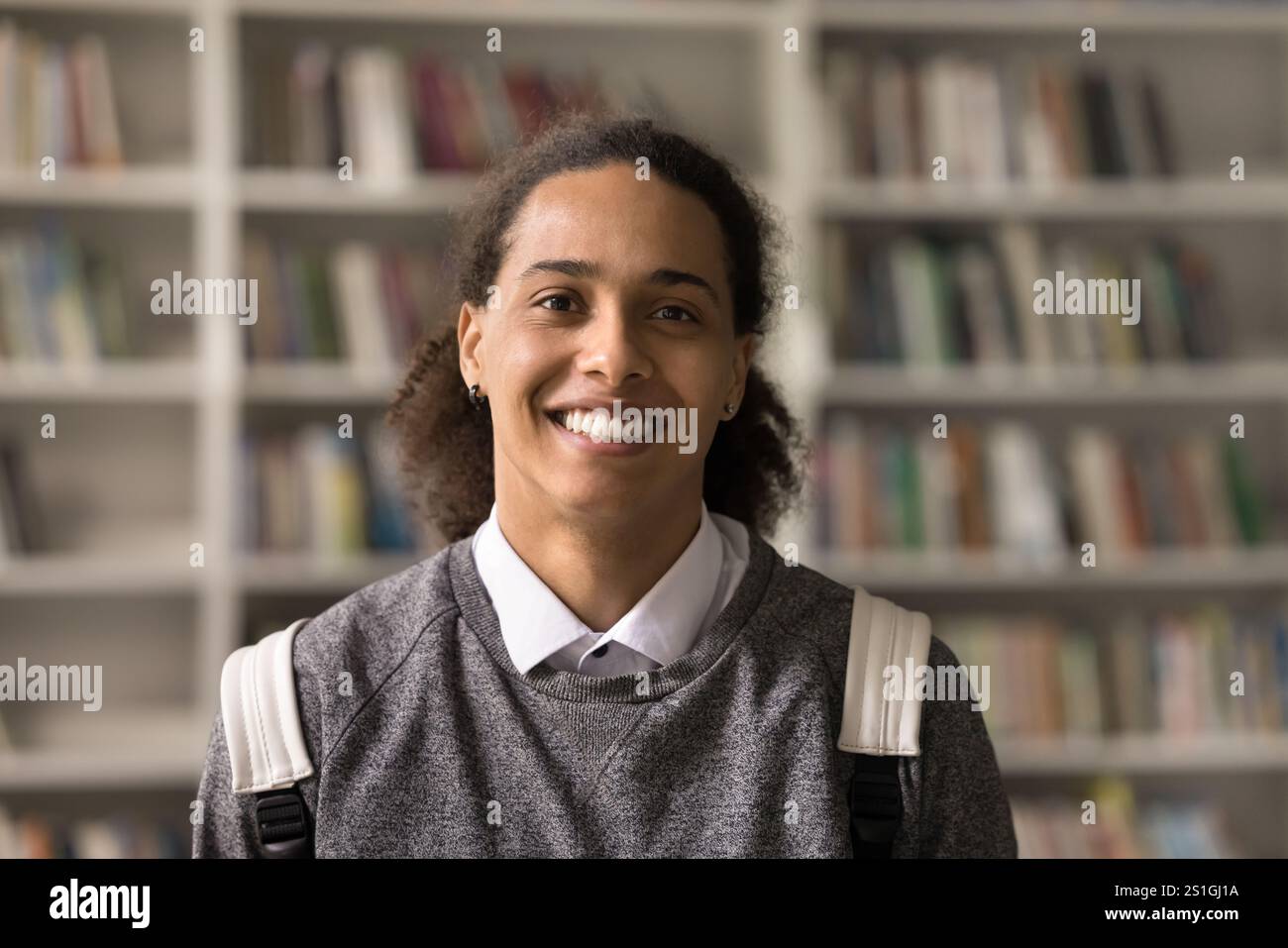 Headshot smiling teen guy student standing in library with backpack Stock Photo