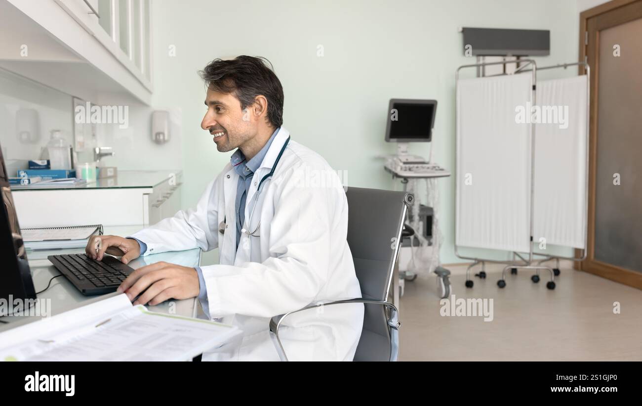Happy middle aged Hispanic doctor man using desktop computer Stock Photo