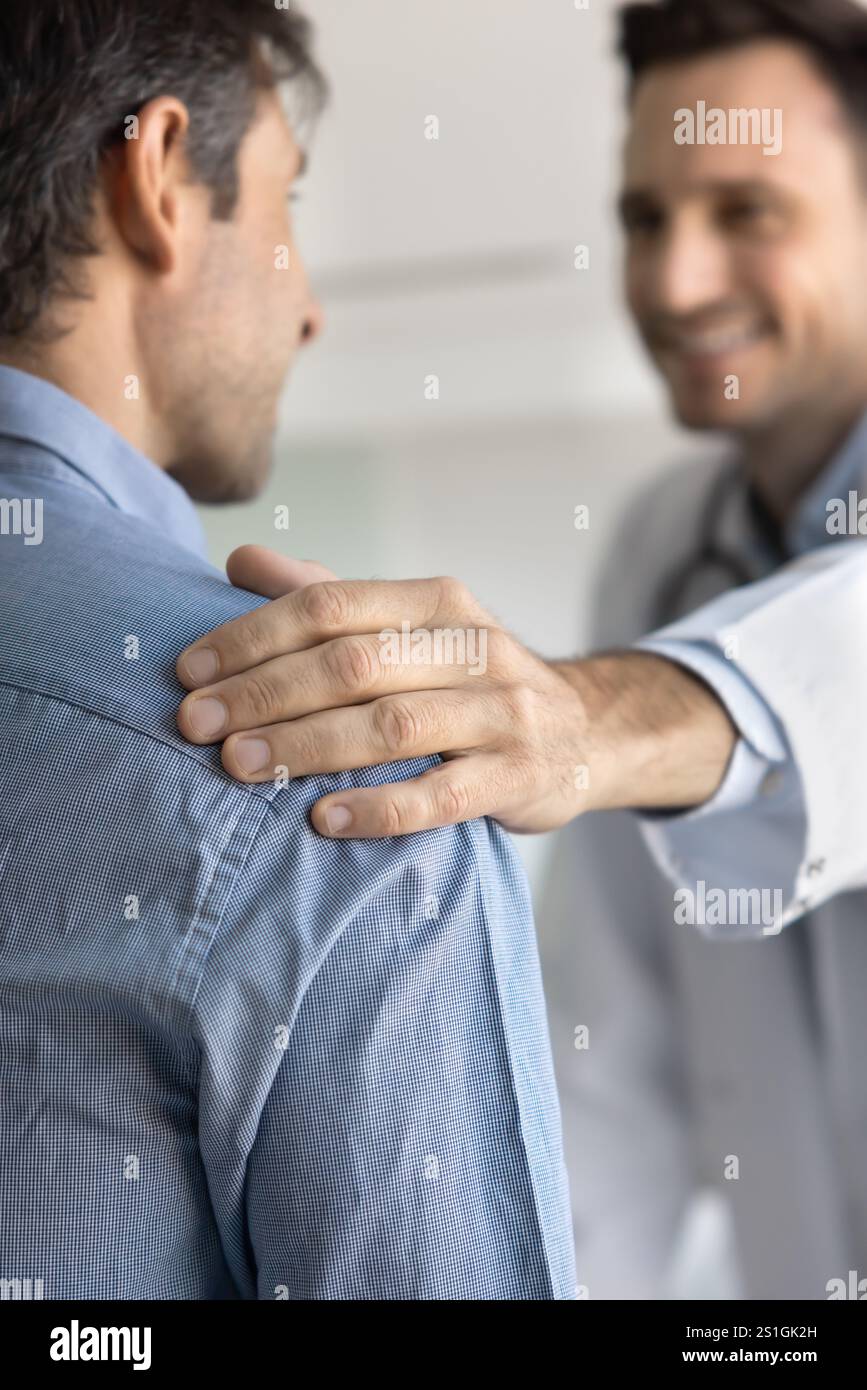 Hand of positive young male doctor touching shoulder of patient Stock Photo