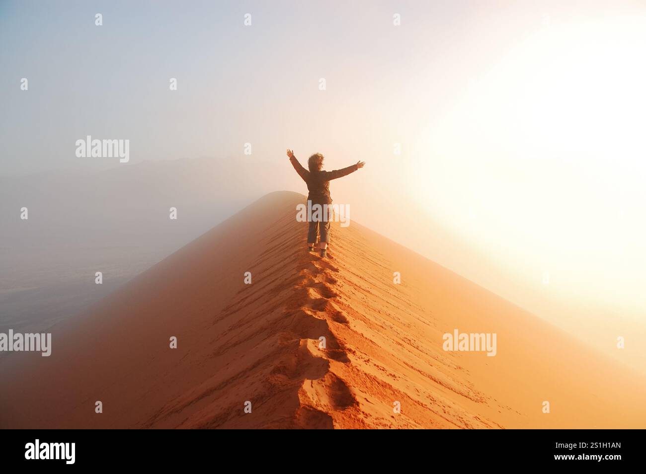 Person standing on top of dune in desert and looking at rising sun in ...