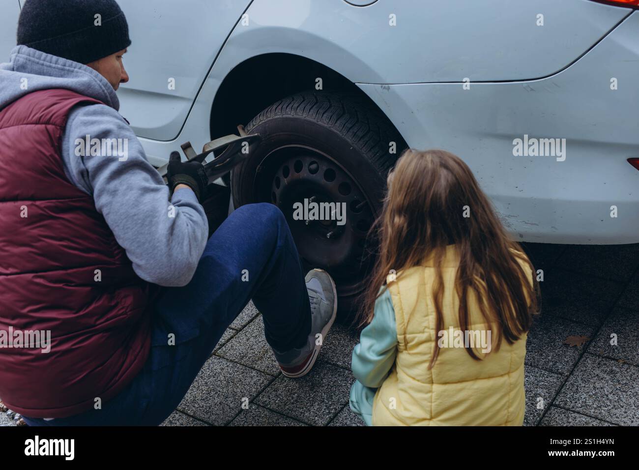 A daughter helps her father change tires on the car, sharing a bonding