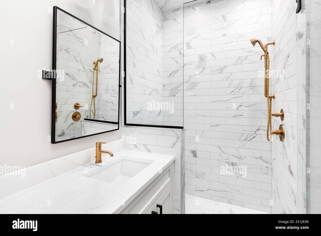 A white bathroom with a marble countertop, gold faucets, black mirror ...