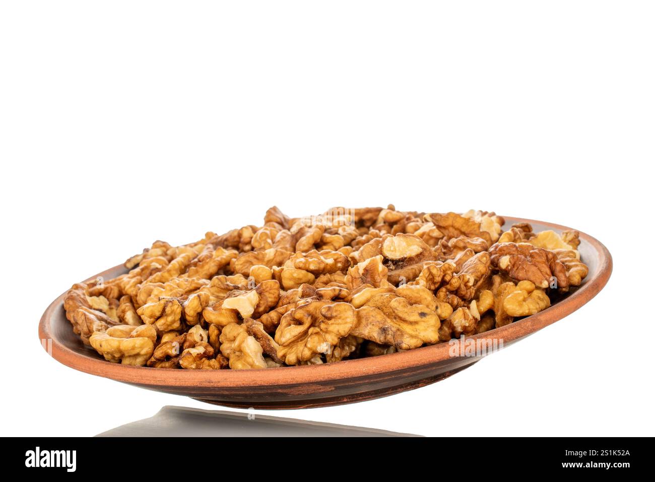 Shelled walnuts on a clay plate, close-up, isolated on a white background. Stock Photo