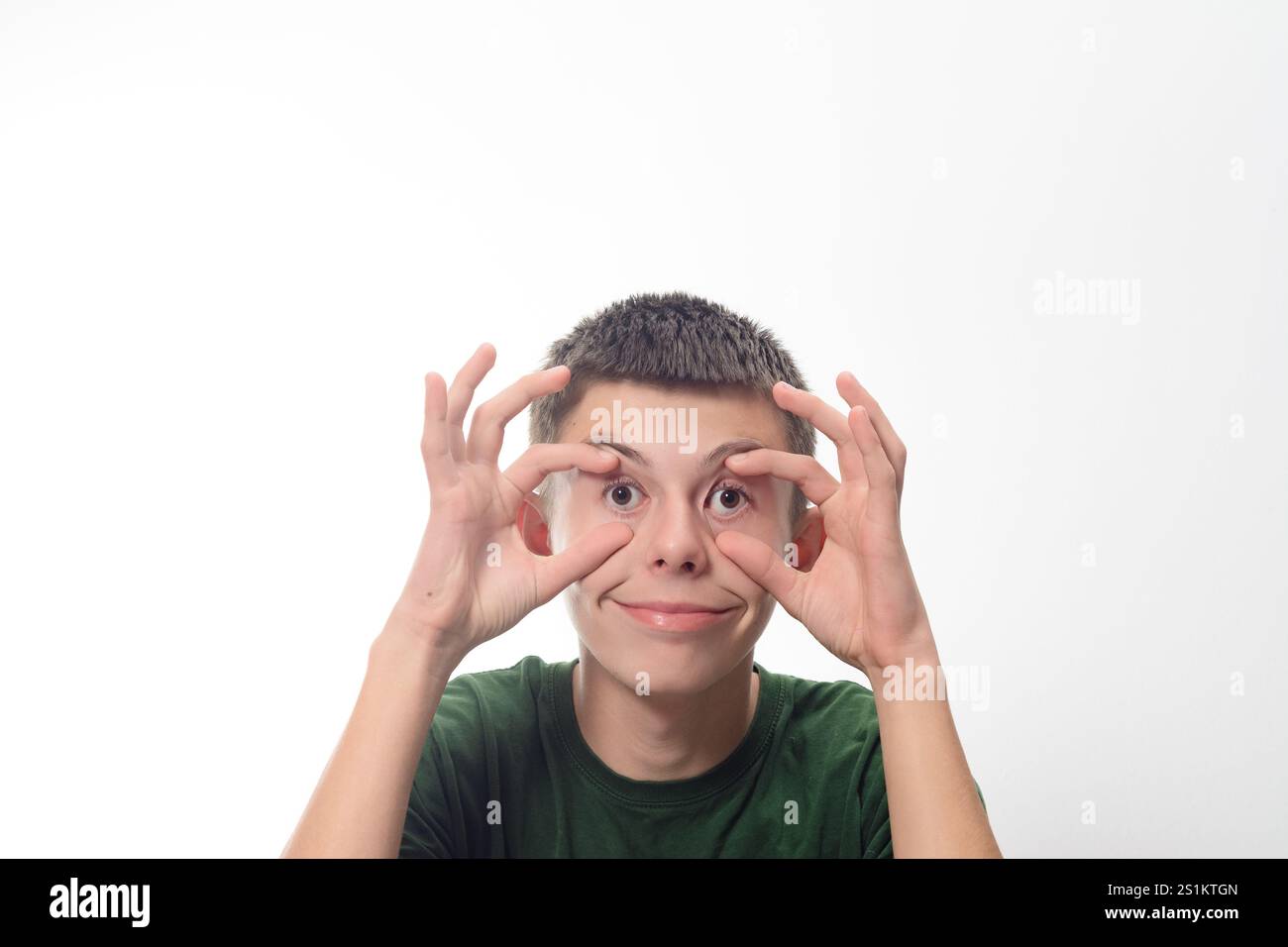 A young boy makes a funny face, playfully covering his eyes with his ...