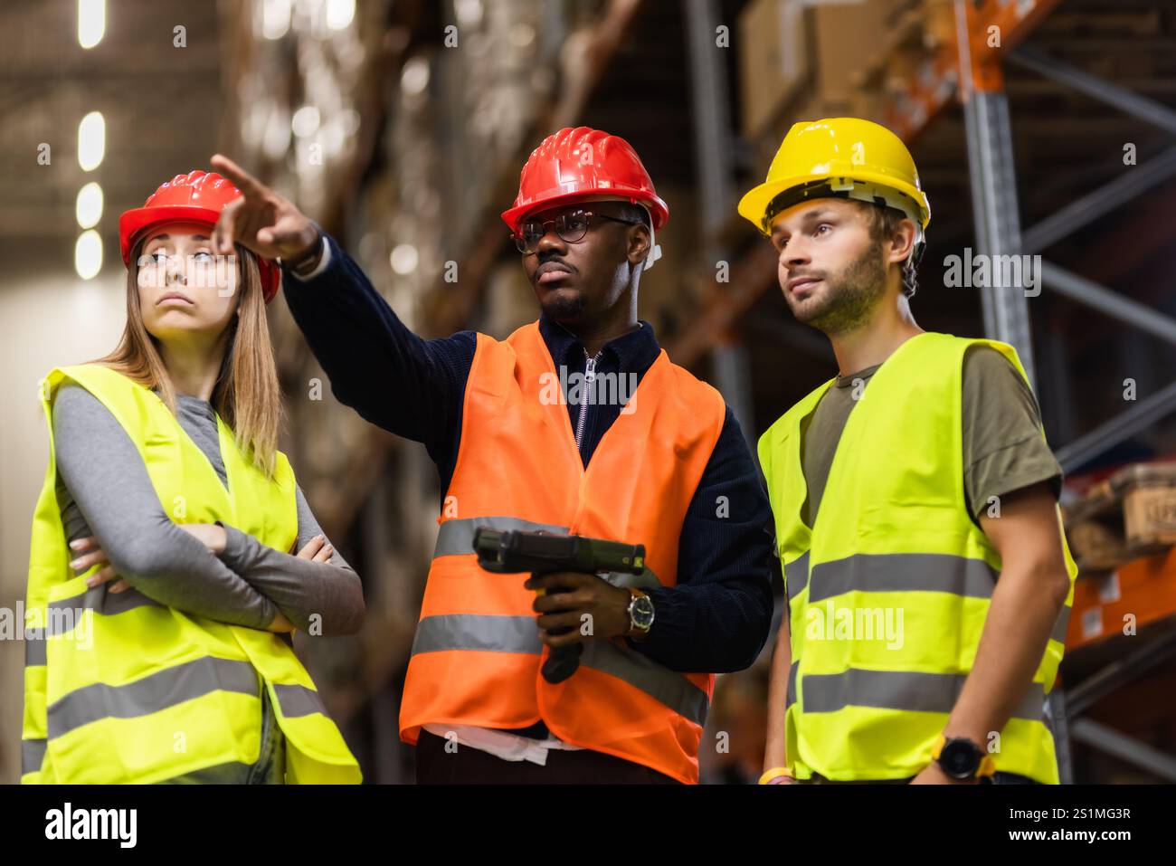 Group of warehouse employees wearing safety helmets and vests, discussing logistics operations. The image captures teamwork, focus, and organization i Stock Photo