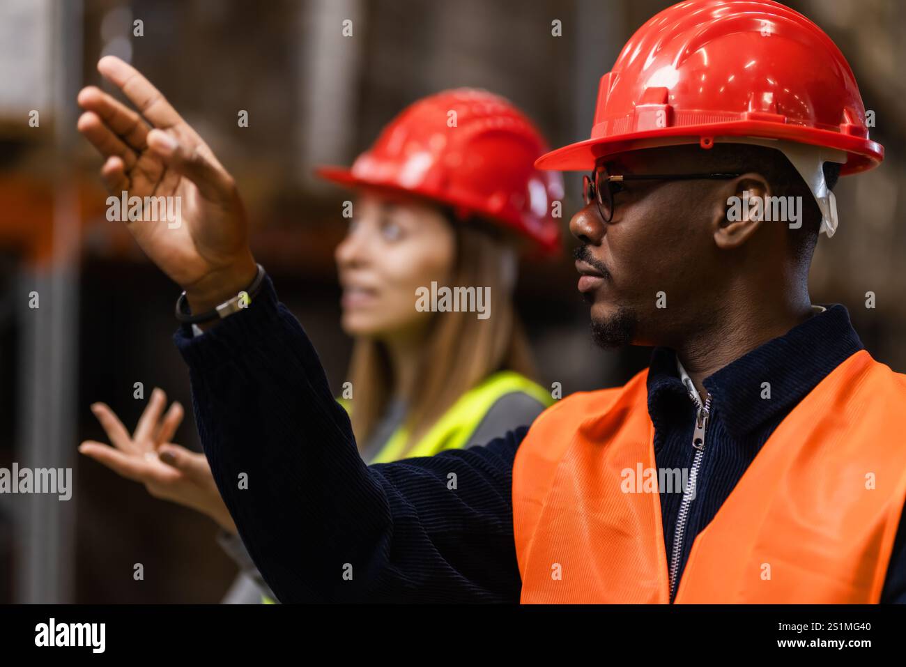 Two construction workers wearing safety vests and helmets communicate effectively on a project site. The image highlights teamwork, safety, and effici Stock Photo