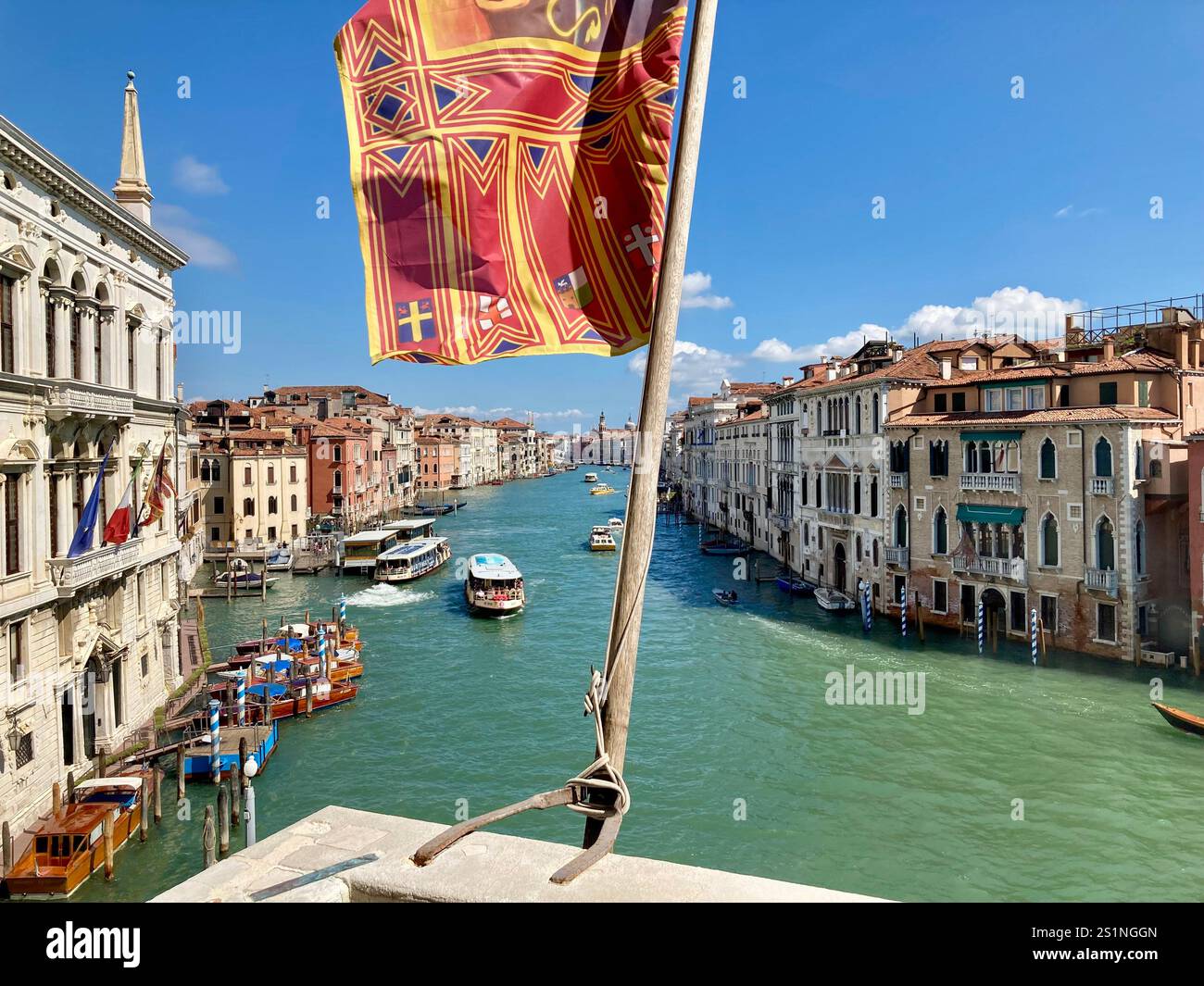 The Venetian flag flying over the Grand Canal, Venice, with motor boats, and palaces, under a blue sky - Smartphone Captured Stock Image