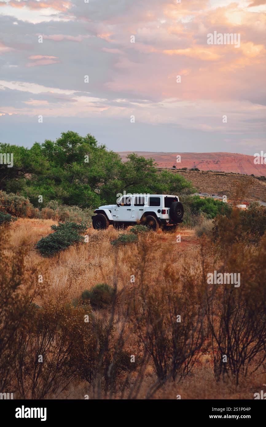 White Jeep Wrangler 392 on a rugged trail, surrounded by golden grass and desert cliffs at sunset Stock Photo