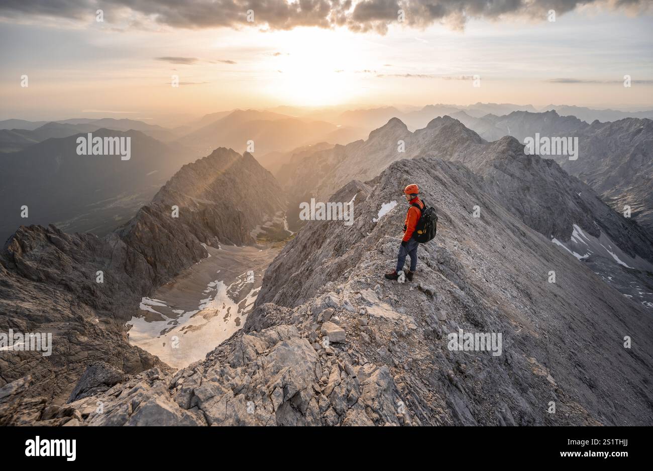 Mountaineer with helmet on a narrow rocky ridge at sunrise, crossing ...