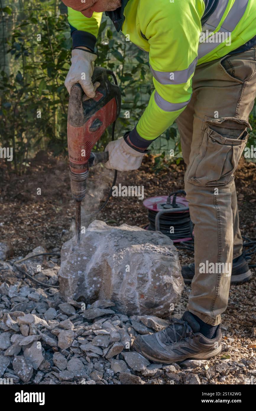 A worker smashes a large concrete block using an electric demolition hammer Stock Photo